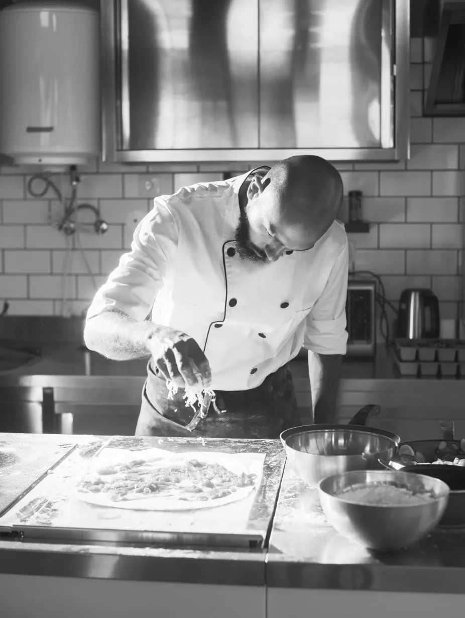 Chef placing cheese on raw pizza bread